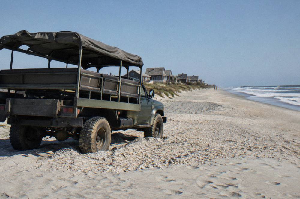 Open-air 4WD tour truck parked on the wide beach north of Corolla